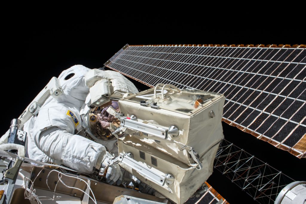An astronaut in a space suit working on electronic equipment near solar panels